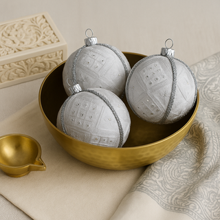 Three Snow Queen Baubles placed in a gold brass bowl, surrounded by a carved ivory box, paisley fabric, and a brass diya for a softly luxurious Indian-inspired setting.
