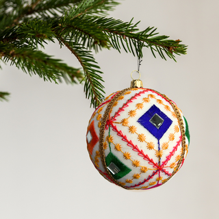 Decorative Christmas ball ornament with embroidered design hanging on a tree branch.