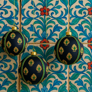 Three Tamasvi Baubles hanging against an ornate tiled backdrop, showcasing their emerald green trim and gold florals in a bold, colourful setting.