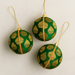 Three green and gold patterned ornaments on a beige background. Luxury handmade bauble in emerald green and gold leaf design, sustainable ornament for Christmas, weddings, and home styling.