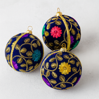Three Mahir embroidered ornaments with floral patterns on a white background. Luxury handmade bauble in deep navy velvet with gold trim and floral embroidery, sustainable ornament for Christmas and weddings