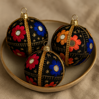 Handcrafted mirrorwork bauble in black with pink, blue, orange, and yellow floral embroidery. Three baubles Sat in a bowl 