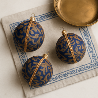 Three blue and gold patterned spherical ornaments on a textured surface with a decorative border.