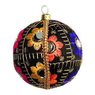 A single 10cm Vimal Bauble made of black fabric, embroidered with vibrant orange and pink flowers, metallic gold thread detailing, and tiny mirrored accents, resting naturally on a warm wooden surface.