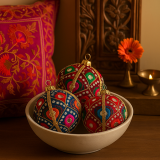 Three Vivaan Baubles, two red and one blue, arranged in a ceramic bowl on a wooden console, surrounded by a kantha cushion and brass diya for a rich, Indian-inspired setting.